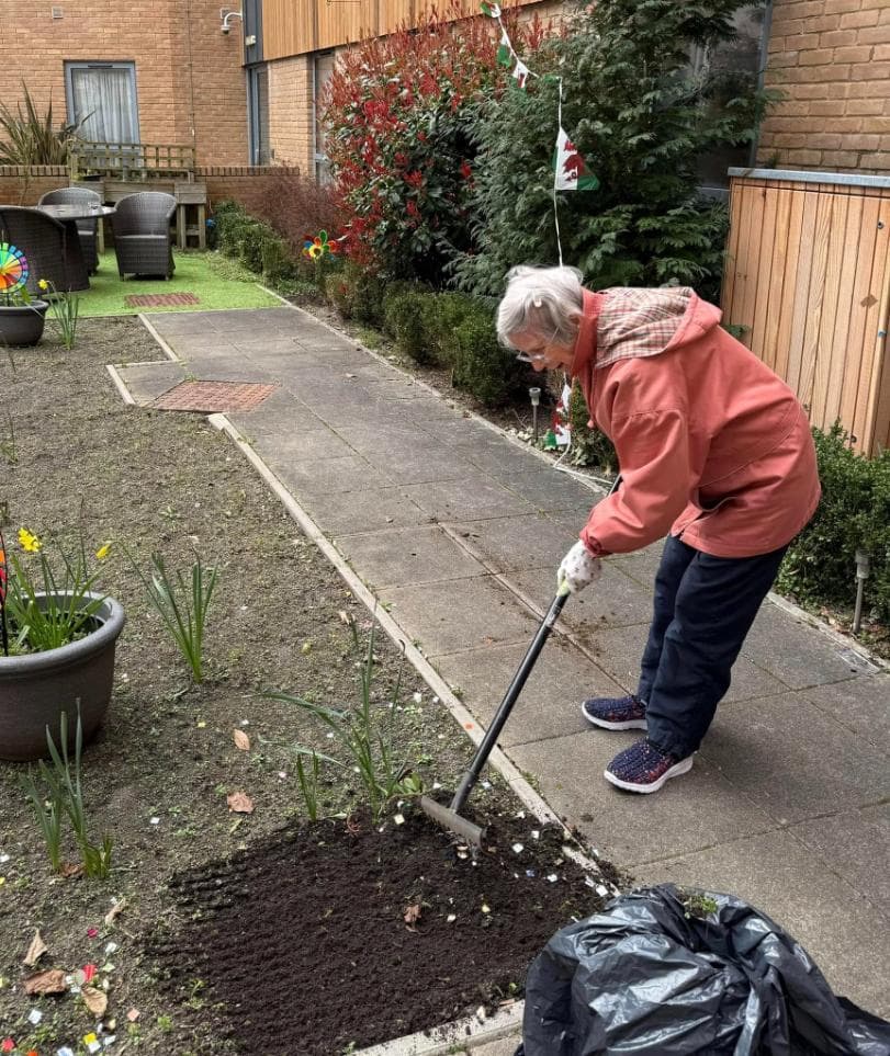 resident in a pink coat raking the soil